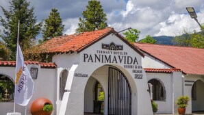 Un edificio blanco con techo rojo, identificado como 'Panimavida Resort & Spa', que presenta una entrada arqueada y un asta de bandera.