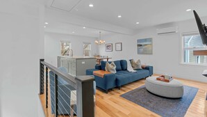 Ein modernes Wohnzimmer mit einem blauen Sofa, einem grauen Hocker und einer Treppe mit Geländer.