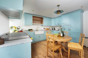 Une cuisine avec des meubles de couleur bleu clair, une table à manger en bois et un luminaire suspendu moderne.