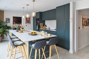 A modern kitchen with teal cabinets, a white island, bar stools, and pendant lighting.