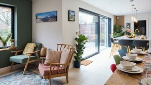 Ein moderner Essbereich mit großem Fenster, einem gedeckten Esstisch und einer Sitzgruppe bestehend aus Stuhl und Sofa.