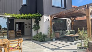 Ein modernes Haus mit einer Terrassenfläche, ausgestattet mit einem Holztisch, Stühlen und einem grünen Sofa.