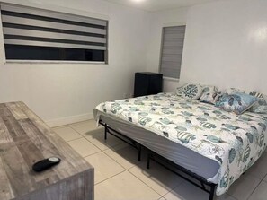 A bedroom with a bed, a desk, a speaker, and a window with blinds. - Casa Luxe Miami (Miami)
