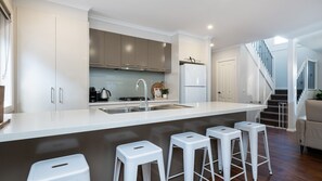 A modern kitchen with a central island, bar stools, a refrigerator, and a staircase leading to a living area. - Parkside Breeze in Rosebud (Rosebud)