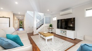 A modern living room with a staircase, a flat-screen TV, and a white sofa. - Parkside Breeze in Rosebud (Rosebud)