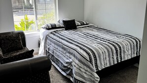 Un dormitorio con una cama, una silla, un ventanal y una lámpara de techo.