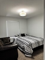 Un dormitorio con cama, una silla, una ventana con persianas y una lámpara en el techo.