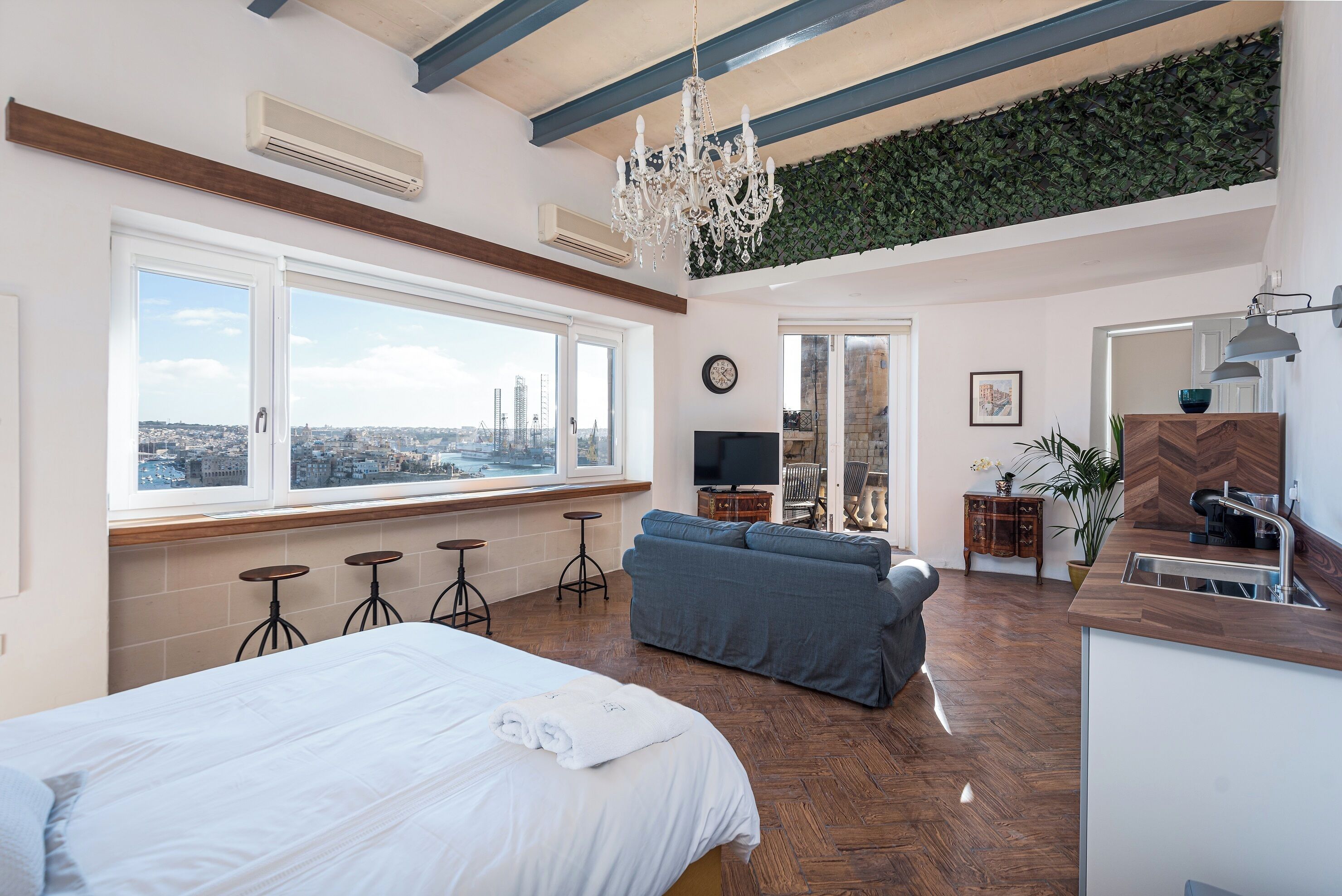 Una habitación de hotel moderna con cama, sofá, zona de comedor, vistas de la ciudad y una pared verde.