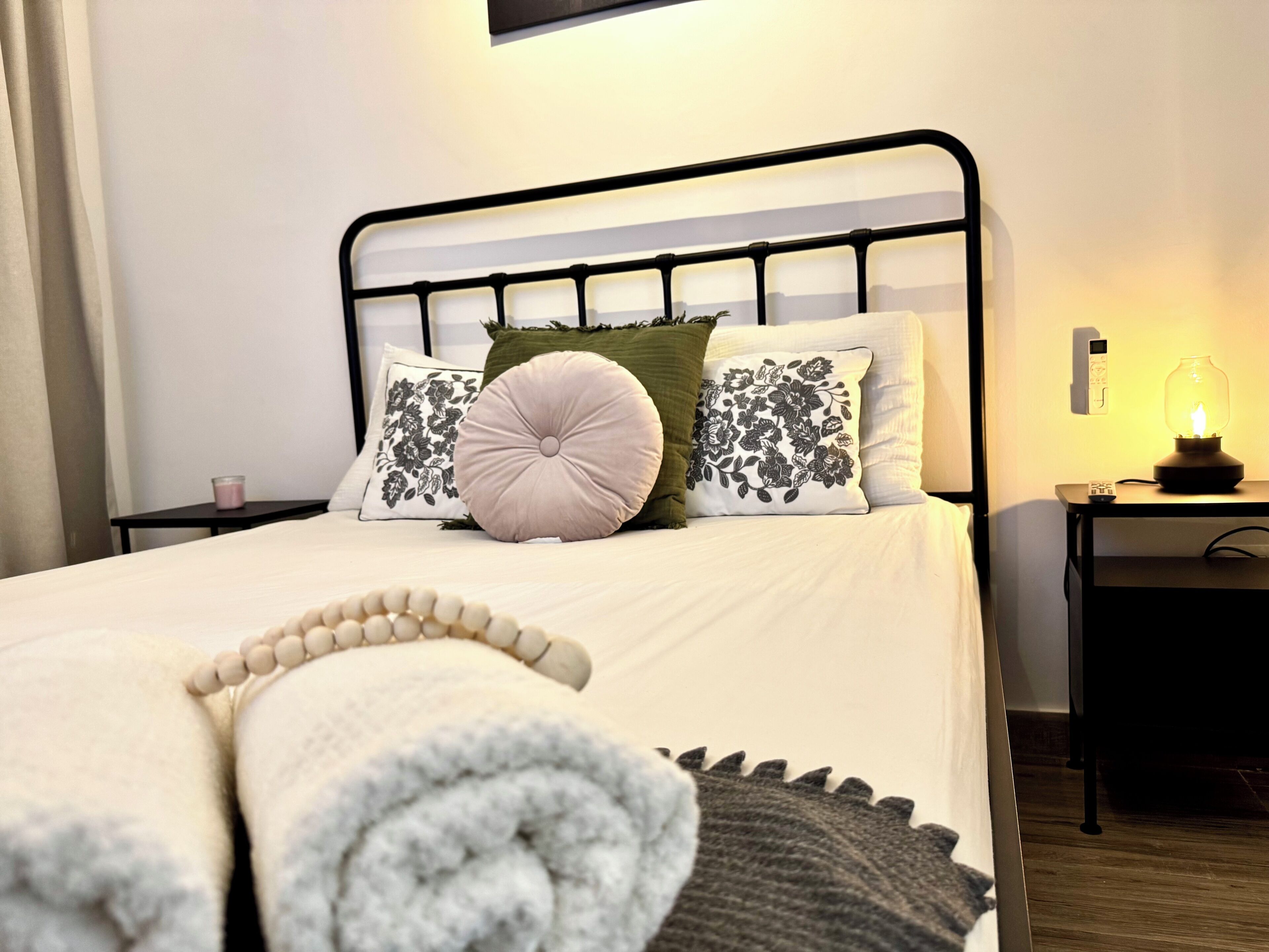 Un lit bien fait, avec une serviette blanche roulée, une tête de lit en métal noir et une table de chevet avec une lampe.