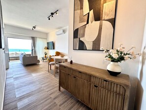 A modern hotel room with a wooden console table, a large abstract painting, a vase with flowers, and a view of the ocean through the window. - LuxuryOceanView Apartment | 16th Floor | 180°Views (Santo Domingo Este)