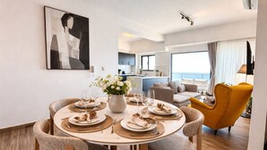 A dining area with a round table set for four, surrounded by chairs, a vase of flowers, and a view of the sea. - LuxuryOceanView Apartment | 16th Floor | 180°Views (Santo Domingo Este)