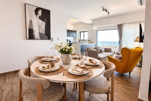 A dining area with a round table set for four, surrounded by chairs, a vase of flowers, and a view of the sea. - LuxuryOceanView Apartment | 16th Floor | 180°Views (Santo Domingo Este)