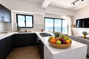 A modern kitchen with a central island, a dining area with a sofa, and large windows offering ocean views. - LuxuryOceanView Apartment | 16th Floor | 180°Views (Santo Domingo Este)
