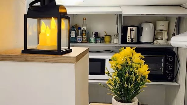 Una cucina con una lanterna nera, un vaso bianco con fiori gialli ed elettrodomestici.