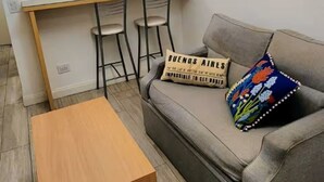 Un ambiente compatto con angolo cottura, divano, tavolino e un quadro appeso.