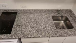 Eine Küche mit einer Granitabdeckung, einer schwarzen Induktionskochplatte und einem Edelstahlspülbecken.