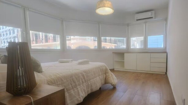 A bedroom with a bed, a bedside table, a lamp, a wardrobe, and a window with a view of buildings. - Centro de Buenos Aires IV (Buenos Aires)