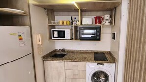 A compact kitchenette with a microwave, toaster, and coffee maker, a washing machine, and a phone on the counter. - Centro de Buenos Aires IV (Buenos Aires)