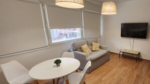 A modern living room with a white table, white chairs, a grey sofa with cushions, a TV, and a bench. - Centro de Buenos Aires IV (Buenos Aires)