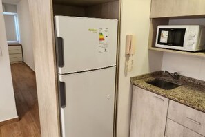 Eine kleine Küche mit einem weißen Kühlschrank, einer Mikrowelle und einer Arbeitsplatte aus Granit.