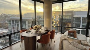 Un comedor moderno con un amplio ventanal que da a vistas de la ciudad, una mesa redonda con vajilla y un sofá con cojines.