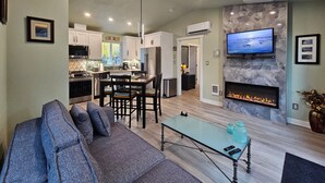 A modern living room with a sofa, a glass coffee table, a fireplace, and a kitchen in the background.
