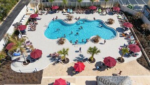 An aerial view of a swimming pool surrounded by sun loungers and umbrellas, with people swimming and relaxing. - Magical & Cozy Disney Retreat at Regal Palms Resort (Davenport)
