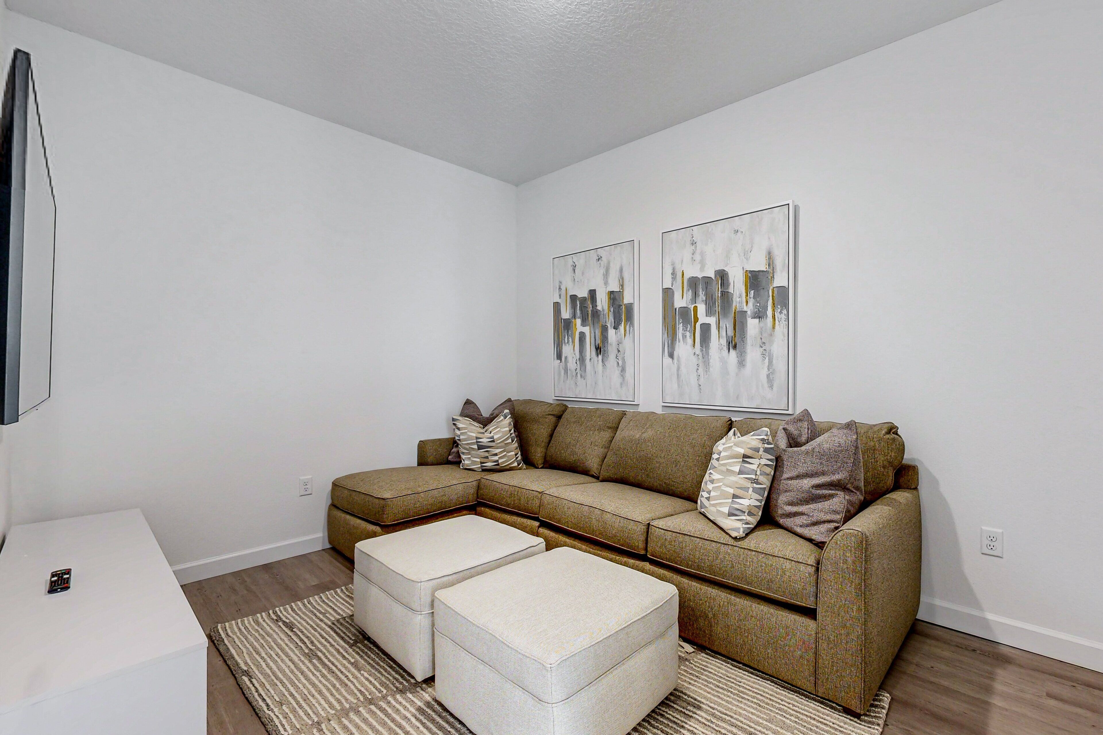 A living room with a sectional sofa, two ottomans, a coffee table, and abstract wall art.