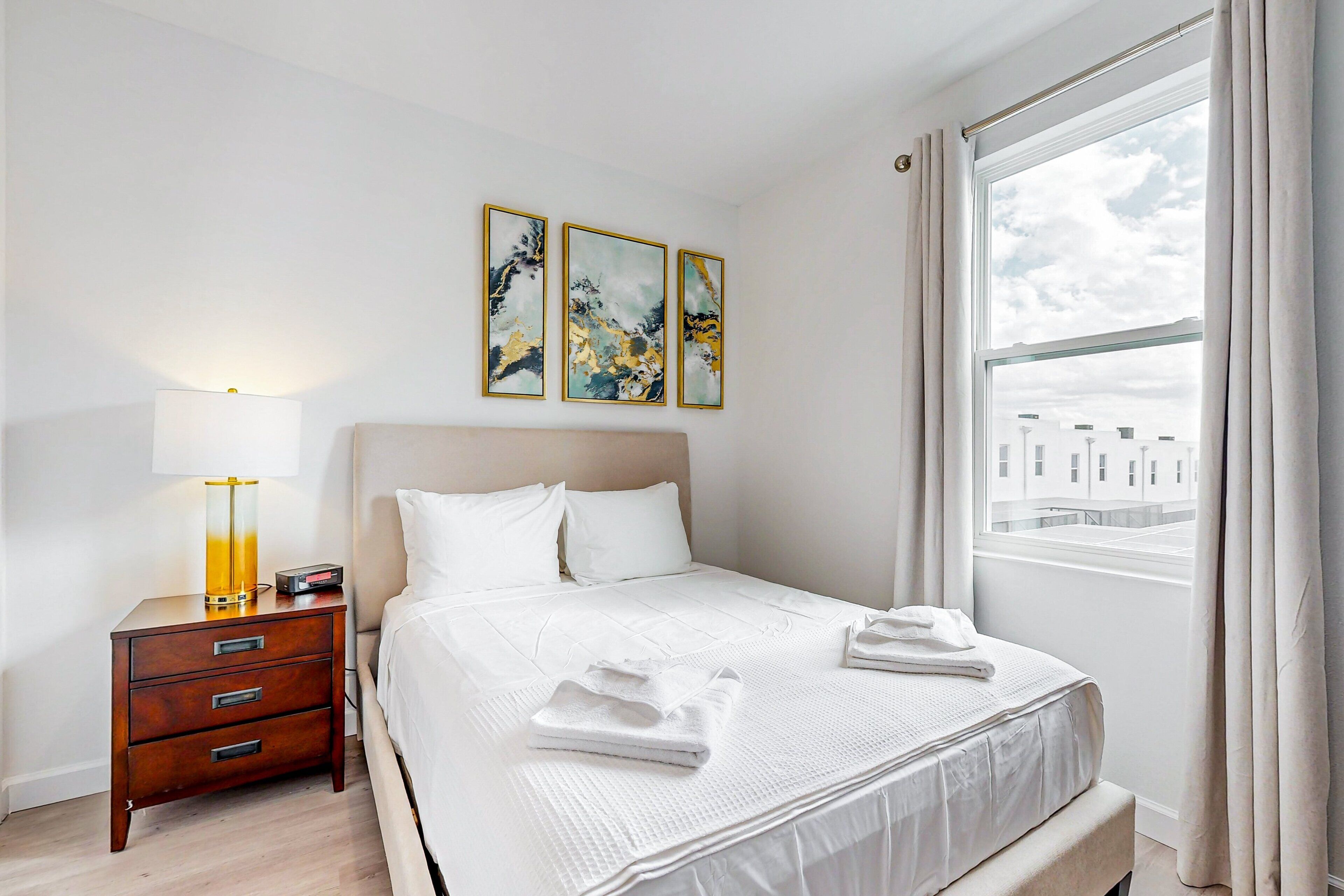 A hotel room with a bed, bedside table, lamp, and artwork on the wall.