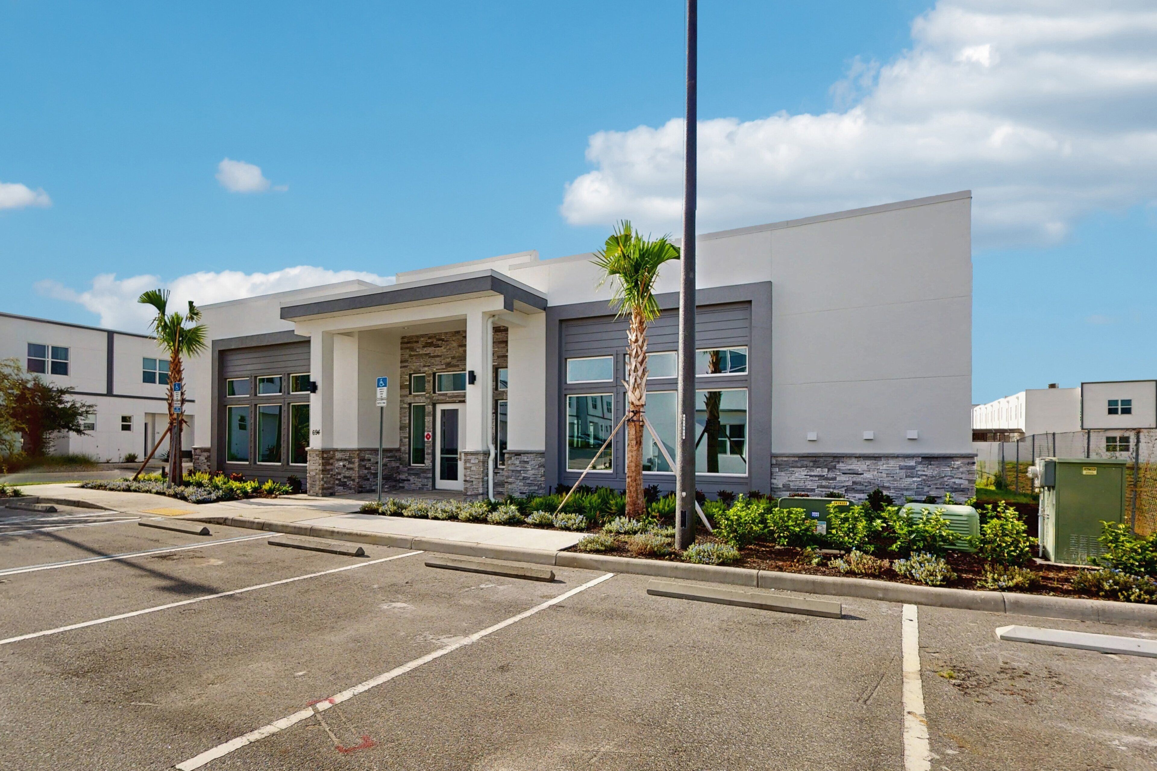 A modern building with a parking lot, a covered entrance, and a landscaped area with palm trees.