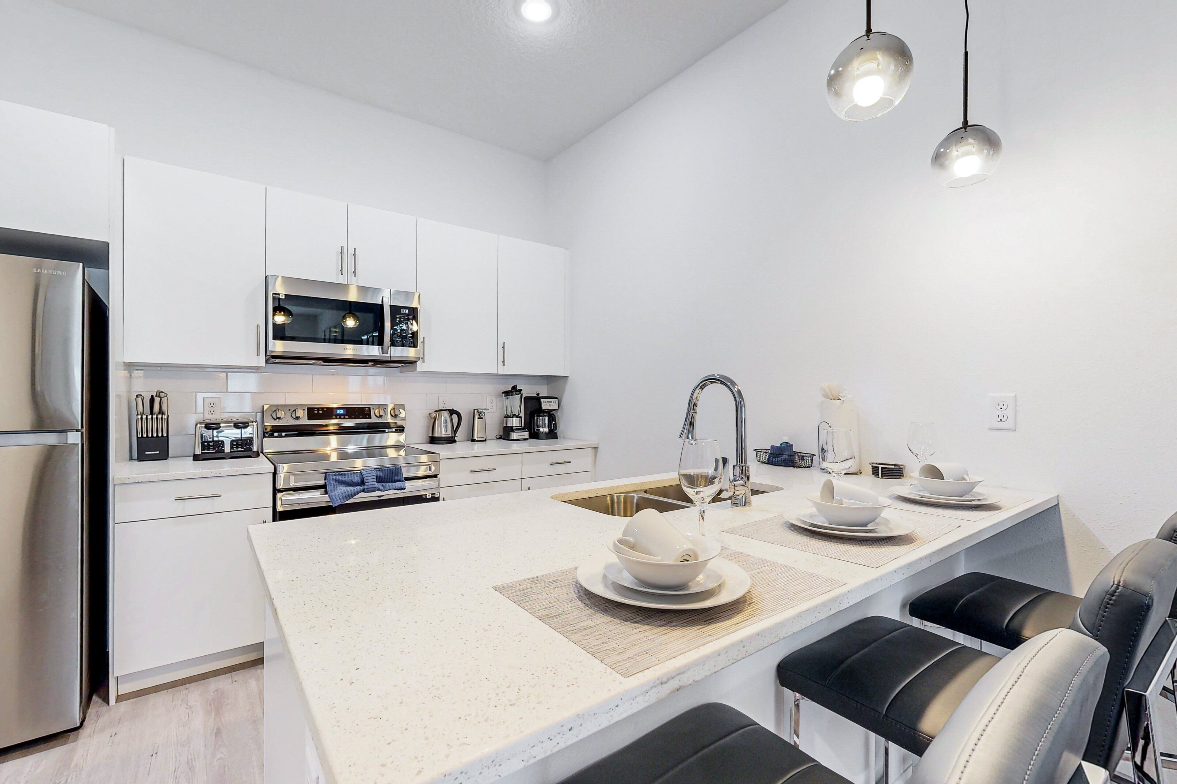 Una cocina moderna con armarios blancos, electrodomésticos de acero inoxidable, una isla central con asientos e iluminación colgante.