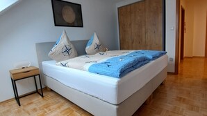 Quarto com cama, guarda-roupa de madeira, mesinha de cabeceira e luminária no teto.