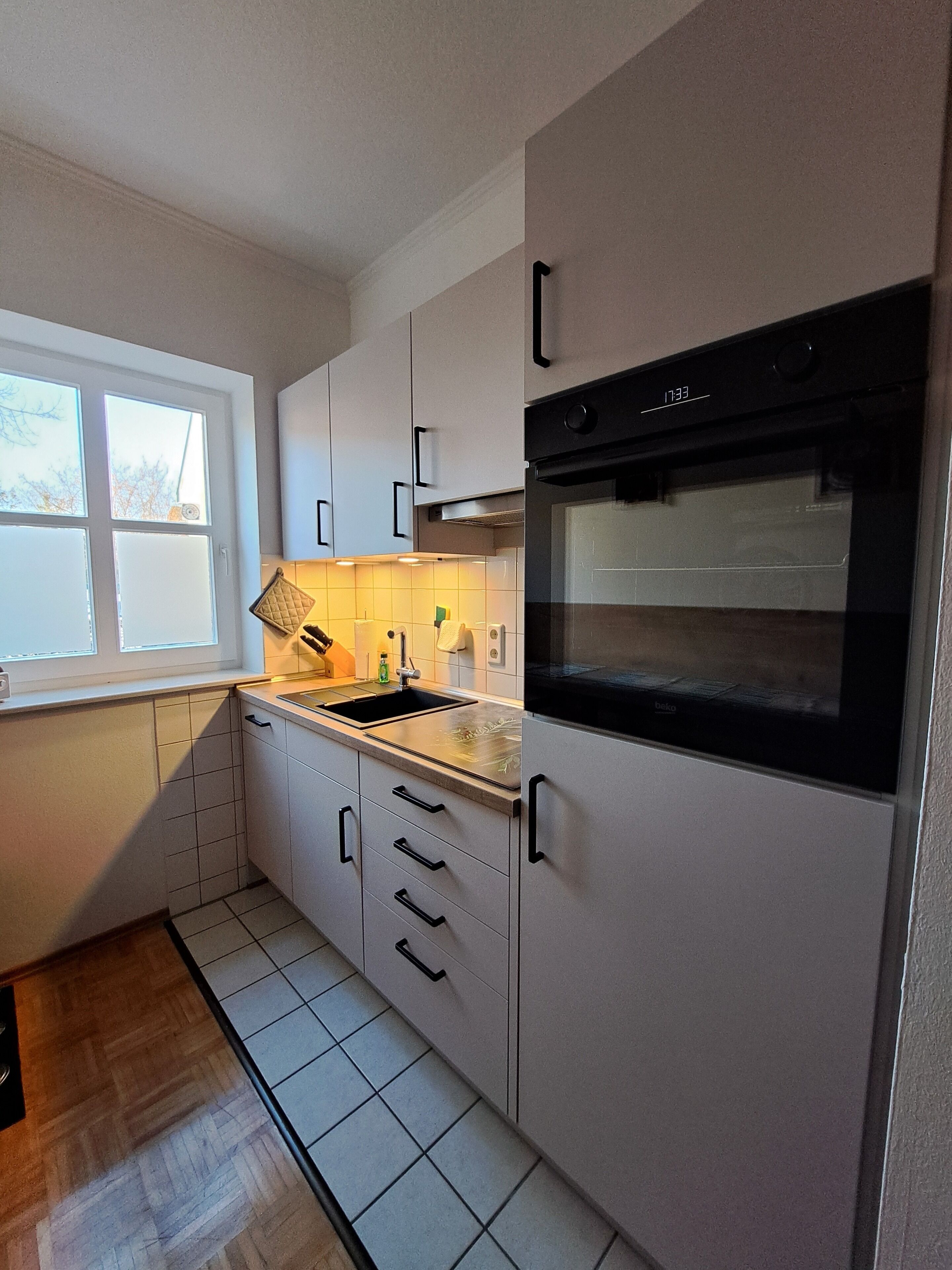 Een moderne keuken met witte kastjes, een zwarte oven en een raam dat voor natuurlijk licht zorgt.