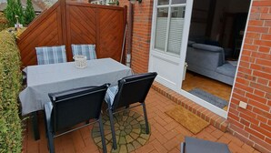 Um pátio com mesa e cadeiras, cerca de madeira e parede de tijolos.