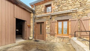 A stone building with wooden shutters, a metal staircase, and a door leading to an interior space. - Le gîte des Bernadettes (APCHAT)