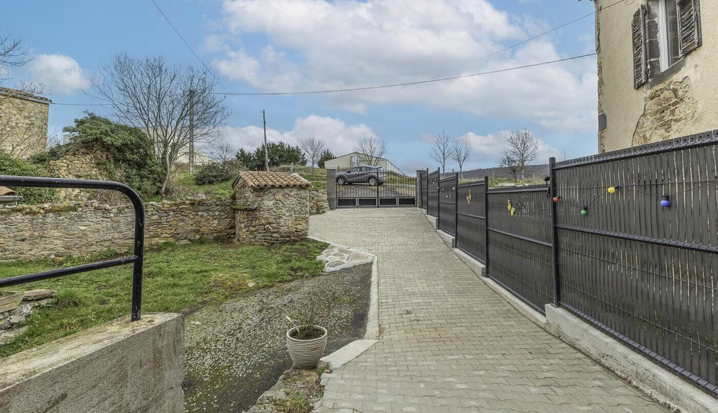 Ein gepflasterter Weg führt zu einem verschlossenen Eingang mit einer Steinmauer und einem Gebäude links.