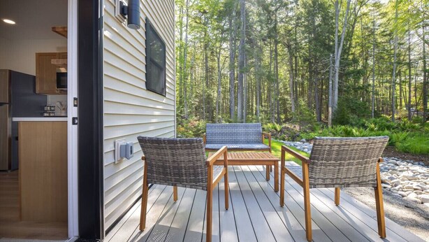 A deck with wicker chairs and a table, overlooking a forested area. - Modern 2025 2 BR Condo in Ellsworth! [Stonewood] (Ellsworth)