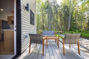 Une terrasse avec des chaises et une table en osier, donnant sur une zone boisée.