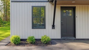 A modern building with a grey exterior, a dark front door, and a small window. - Modern 2025 2 BR Condo in Ellsworth! [Stonewood] (Ellsworth)