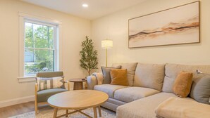 A living room with a sofa, a round coffee table, a lamp, and a painting on the wall. - Modern 2025 2 BR Condo in Ellsworth! [Stonewood] (Ellsworth)