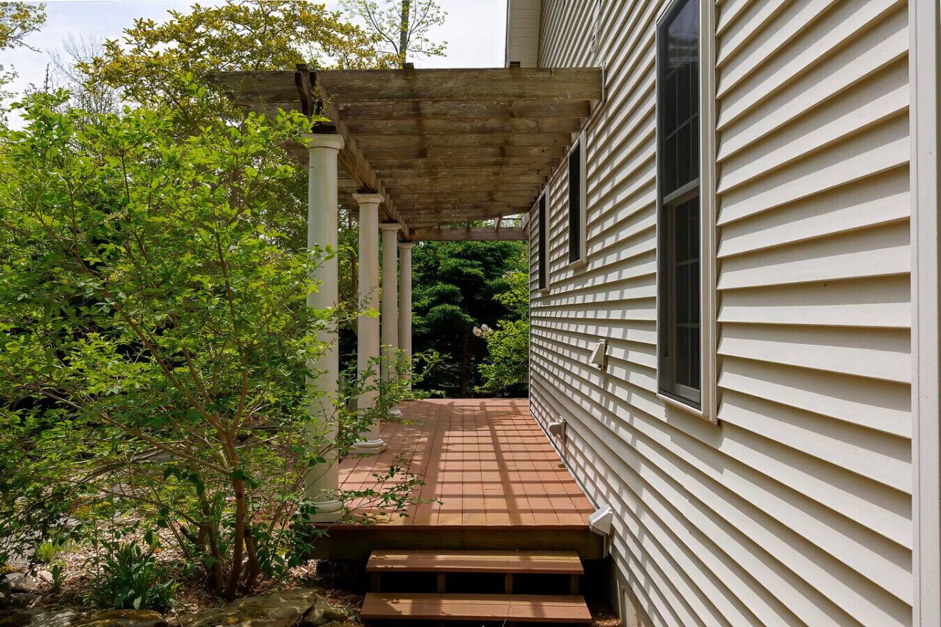 Un porche cubierto con un banco de madera, una pérgola de madera y una casa con revestimiento.