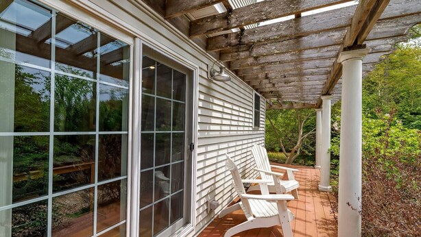 Une véranda couverte avec une porte-fenêtre coulissante, des chaises en bois peintes en blanc et une structure en forme de pergola.