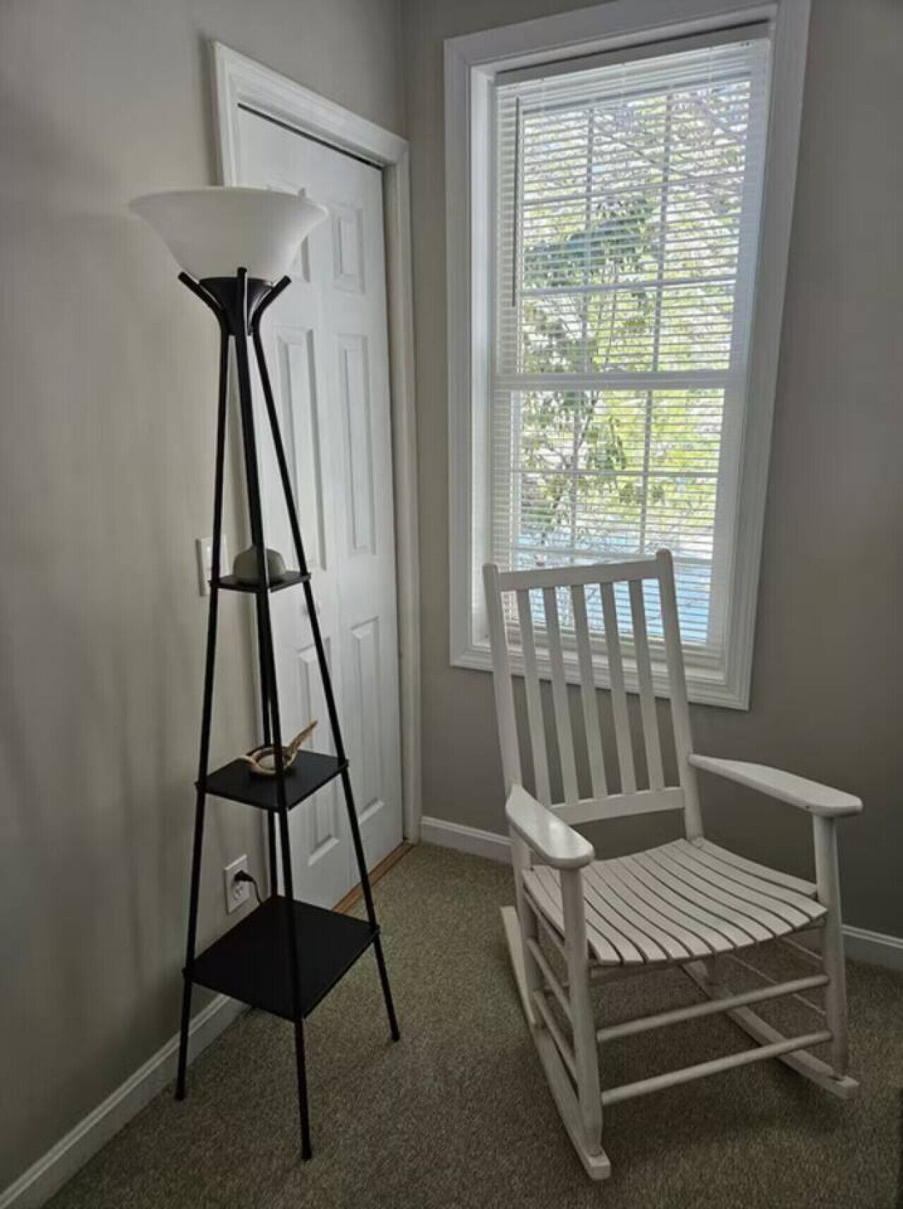 A room with a white chair, a black floor lamp, and a window with blinds.