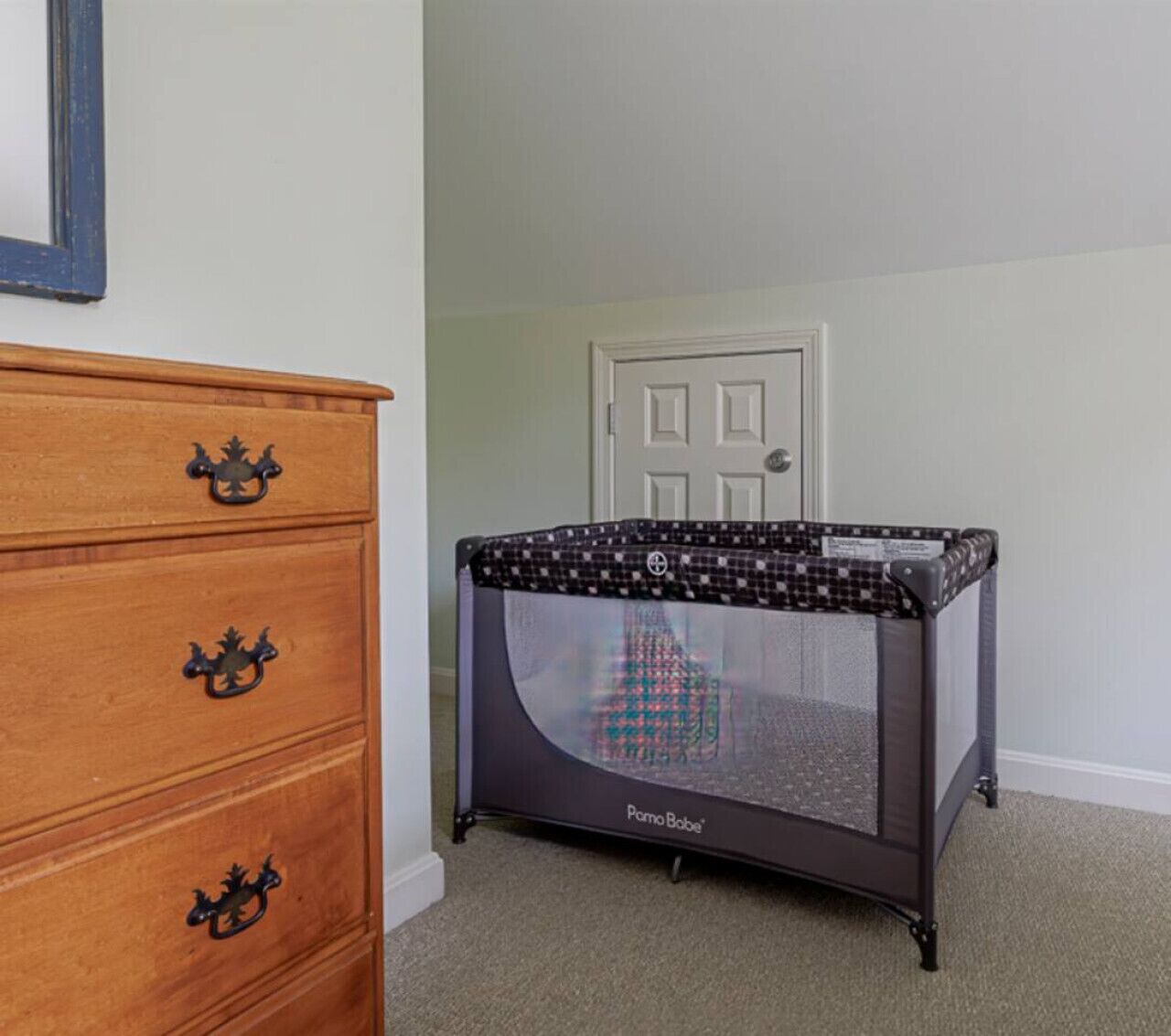 A room with a wooden dresser, a baby playpen, and a door.
