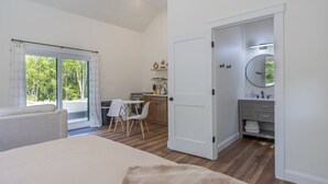 Et soveværelse med en stor seng, et spiseområde med stole, et køkken med komfur og et badeværelse med et spejl.