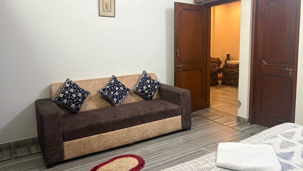 Quarto com sofá marrom, almofadas estampadas, tapete vermelho e bege, e cama com manta estampada.