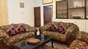 Uma sala de estar com sofás estampados, uma mesa de centro e um aparador com portas de vidro.