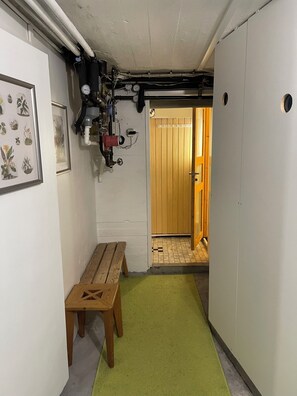 A narrow hallway with a wooden bench, a green mat, and a door leading to a room with a wooden floor.