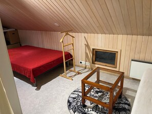 Une chambre avec un lit rouge, une échelle en bois, une petite table, un téléviseur et un radiateur.