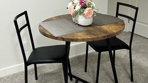 Una mesa redonda con tapa de madera, dos sillas negras y un jarrón con flores.
